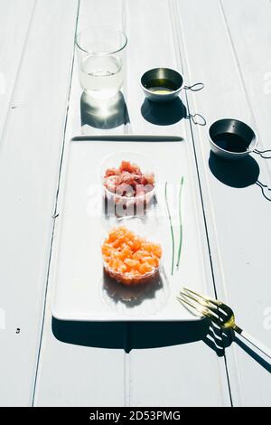 Fisch Tartare, Lachs und Thunfisch auf einem weißen rechteckigen Teller über einem Holztisch.natürliches Licht, Frontalansicht über einer weißen Tafel. Stockfoto