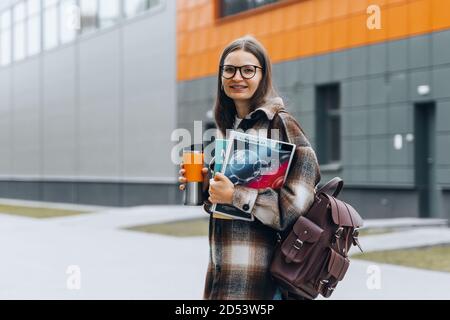 Porträt von jungen glücklichen Studenten hält Bücher Kaffee lächelnd nach bestandenen Prüfungen. Intelligente Frau auf dem Universitätsgelände. College-Leben. Teenanger in Zahnspangen, Stockfoto