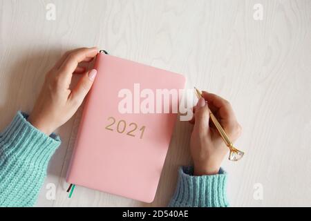 Frau sitzt in gestricktem warmen Pullover mit Koralle gefärbt 2021 Tagebuch auf dem Tisch Stockfoto