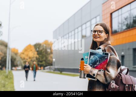 college Studentin mit Buch, Kaffee lächelnd zu Fuß auf dem Universitätscampus. Glückliche Frau in Zahnspangen Brille. Bildung Lernen High School Konzept. Stockfoto