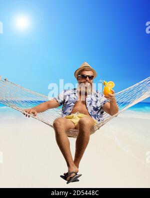 Blonde bärtige Kerl sitzt auf einer Hängematte Schaukel mit einem Cocktail am Strand Stockfoto
