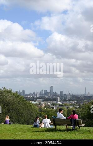 Menschen unterhalten sich in kleinen Gruppen auf Parliament Hill, London, Großbritannien, mit Blick auf London City Sky Line. Stockfoto