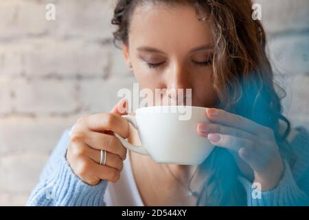 Glückliche junge Frau in gestrickten warmen Pullover mit Händen halten Eine Tasse gesunden heißen blauen Kaffee Latte Stockfoto