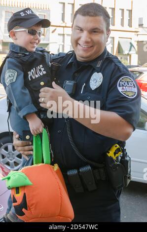 Ein Polizist hält seinen Sohn, der als Polizist für Halloween gekleidet ist, während Trick-oder-Behandlung in der Innenstadt, 31. Oktober 2011, in Columbus, Mississippi. Stockfoto