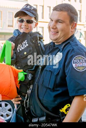 Ein Polizist hält seinen Sohn, der als Polizist für Halloween gekleidet ist, während Trick-oder-Behandlung in der Innenstadt, 31. Oktober 2011, in Columbus, Mississippi. Stockfoto