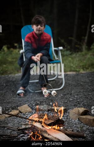 Kleiner Junge, der Marshmallows auf einem Metallstab über einem Feuer röstet. Stockfoto