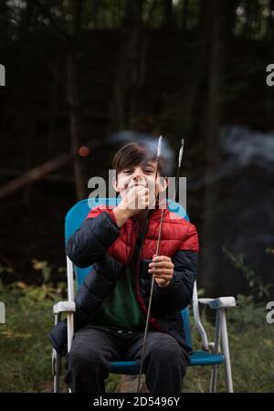 Kleiner Junge, der draußen eine Marshmallow von einem Metallstab isst. Stockfoto