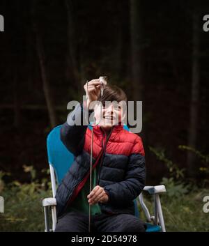 Kleiner Junge, der draußen einen Marshmallow von einem Metallstab abnimmt. Stockfoto