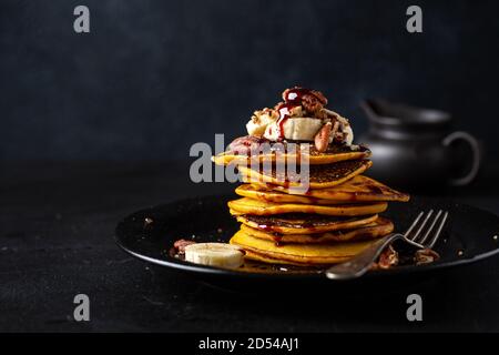 Leckere, appetitliche Kürbispfannkuchen mit Banane, Nüssen und Karamell auf dem Teller serviert. Nahaufnahme Stockfoto