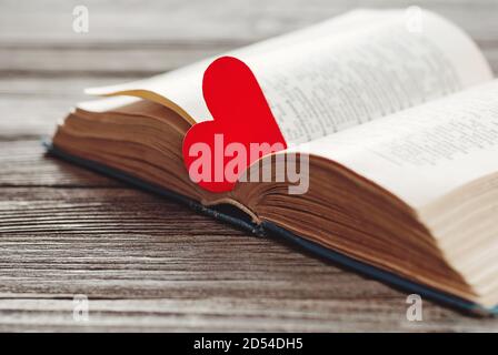 Offenes Buch mit rotem herzförmigem Papierlesezeichen auf Holz Hintergrund Stockfoto