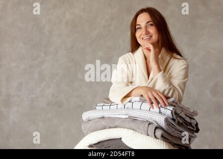 Junge Frau mit schönen Lächeln in warmen beige Robe ist Lehnt sich auf einen Stapel gefalteter Bettlaken Stockfoto