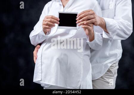 Schwangere Paar hält Ultraschall Schwangerschaft Testergebnis mit schwarzem Hintergrund Stockfoto
