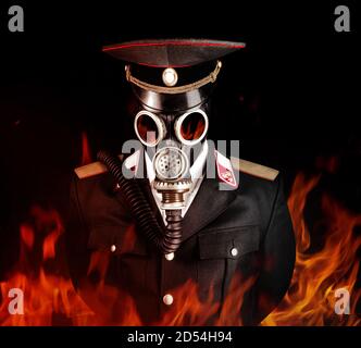 Foto eines postapokalyptischen Militäroffiziers in Uniform Anzug und Spitzenmütze stehend in sowjetischer Gasmaske in Feuer. Stockfoto