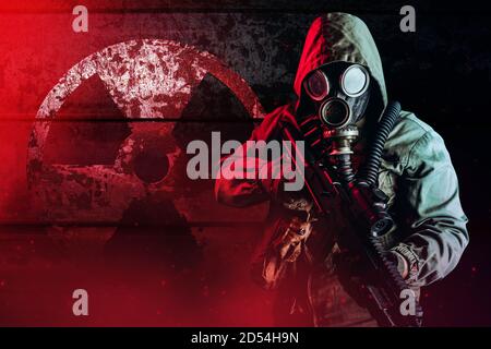 Foto eines postapokalyptischen Stalker Soldaten in Gasmaske Und Kapuzenjacke hält Gewehr und steht auf dunkel rostig Metallwand mit Strahlungszeichen und RE Stockfoto