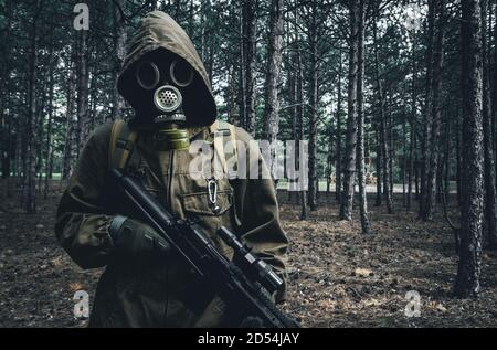 Foto eines nuklearen Kriegsstalker Soldat stehend und posiert in sowjetischer Gasmaske, Rucksack mit Gewehr in Wäldern. Stockfoto