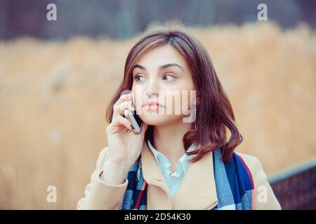 Skeptische Frau am Telefon zu entscheiden, was im Freien zu beantworten park im Herbst auf dem Hintergrund Stockfoto