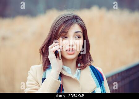 Skeptische Frau am Telefon zu entscheiden, was im Freien zu beantworten Im Parkhintergrund Stockfoto