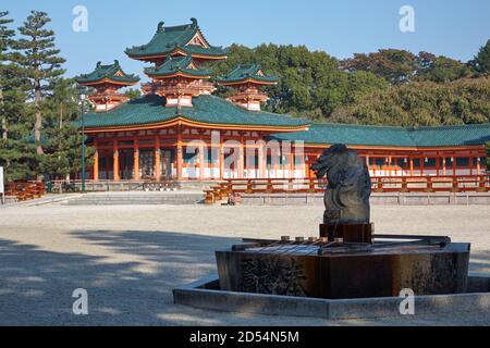 Drachenstatue über dem Wasserwaschbecken für zeremonielle Reinigung (Tsukubai) mit Zinnoberrot Byakko-ro Turm des Heian-jingu Schreins auf dem Hintergrund. Stockfoto