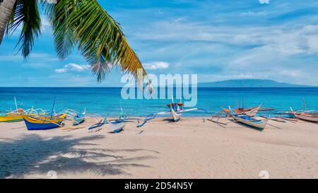 Traditionelle Outrigger Boote an einem wunderschönen weißen Sandstrand, mit türkisfarbenem Wasser und blauem Himmel im Erholungsgebiet von Puerto Galera, Philippinen. Stockfoto