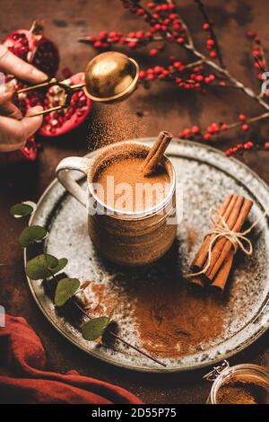 Menschliche Hand gießt Zimtpulver zu türkischen Heißgetränk Salep Stockfoto