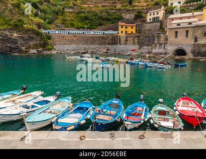 Schöner Blick auf den Hafen von Vernazza in der Küstenregion Cinque Terre. Kleine Boote, schwimmend auf seichtem türkisfarbenem Wasser, sind bis zum Pier und in... Stockfoto