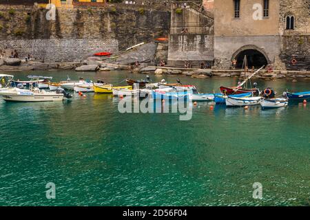 Schöne Aussicht auf kleine Boote im flachen türkisfarbenen Wasser, verankert im Hafen von Vernazza mit alten Gebäuden im Hintergrund. Es ist eines der... Stockfoto