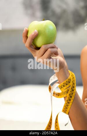 Frau hält einen frischen gesunden grünen Apfel in der Hand Mit einem Maßband um ihren Arm gewickelt in einem Diät und Gewichtsverlust Konzept in der Nähe Stockfoto