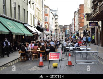 Menschenmenge mit Covid-19 temporäre Beschränkungen Schild auf Old Compton Street. Viele Straßen im Zentrum von London wurden für den Verkehr gesperrt, um Sitzmöglichkeiten im Freien für Bars und Restaurants während der Pandemie zu ermöglichen. Stockfoto