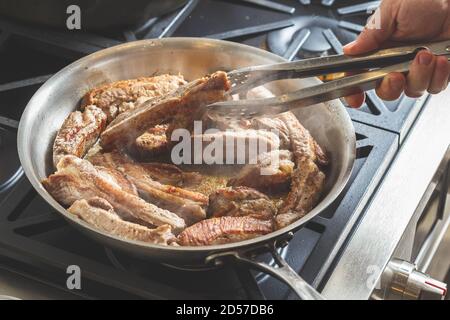Man's Hand Braten Schweinefleisch Spare Ribs Fleisch auf einer Stahlpfanne. Zubereitung des Abendessens Stockfoto