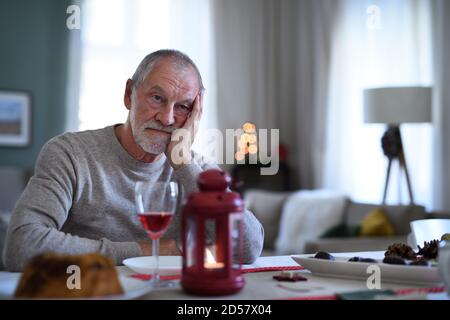 Einsamer älterer Mann mit Wein sitzen an den Tisch drinnen zu Weihnachten, Einsamkeit Konzept. Stockfoto