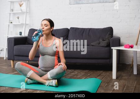 Schwangere Frau sitzt auf Fitness-Matte, während Wasser aus trinken Sportflasche Stockfoto