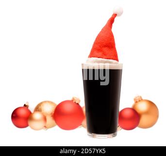 Volles Pint Glas dunkles Bier oder stout Ale mit Weihnachtsmann roten Hut auf und verschwommen weihnachtskugeln in Hintergrund auf weiß Stockfoto