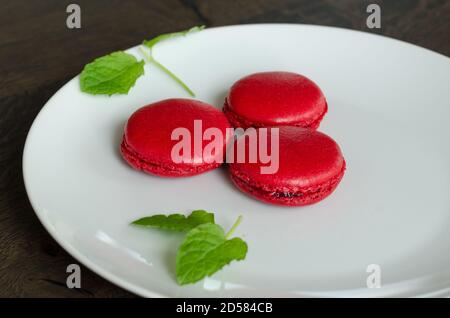 Hausgemachte Beeren roten Macarons in einem weißen Teller, als Dessert für die Zeit im Café zu Hause serviert. Home Spaß Backen, Quarantäne-Ideen Stockfoto