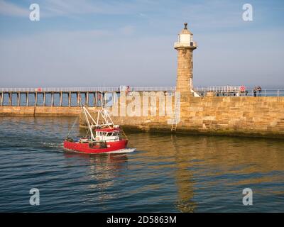 Ein rotes Fischerboot kehrt nach Whitby Harbour an der Ostküste von North Yorkshire, England, Großbritannien zurück - aufgenommen am Ende des Nachmittags Stockfoto