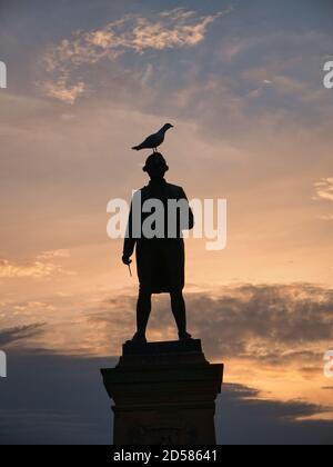 Die Bronzestatue von Captain James Cook in Whitby, North Yorkshire, Großbritannien, wurde an einem späteren Sommerabend gegen die untergehende Sonne geschildet Stockfoto