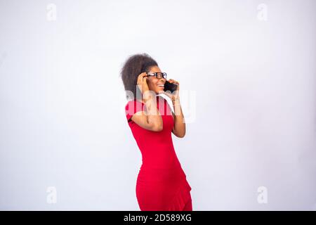 Aufgeregt afrikanische Frau trägt ein rotes Kleid und Brille machen Ein Anruf Stockfoto