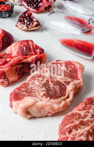 Beef Cuts Chuck Eye Roll, Top Blade, Rumpsteak mit Rotwein in Glas und Flasche, Kräuter und Granatapfel. Bio-Fleisch. Weißer strukturierter Hintergrund Stockfoto