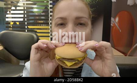 Junge Frau essen Hamburger in Fast-Food-Café. Stockfoto