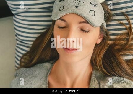 Ziemlich lange Haare Junge Frau im schlafen auf Bett. Stirnschlafmaske. Graue Farben. Stockfoto
