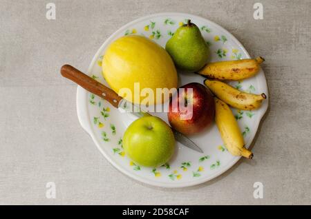 Obstschale mit Birne, rotem Apfel, grünem Apfel, Banane und Kanarienmelone auf einem Teller angeordnet. Studioaufnahme Stockfoto