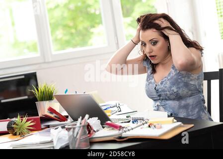 Überarbeiteter junger Geschäftsfrau, die an einem unordentlichen Schreibtisch sitzt Stockfoto