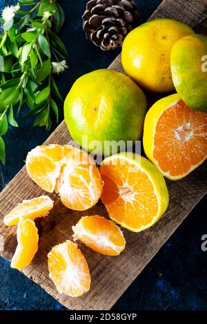 Reife Mandarine Frucht geschält offen und legen auf alten rustikalen Look Holz mit Gruppe von Mandarinen Früchte und Blätter. Winterfrüchte. Stockfoto