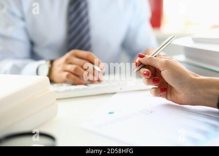 Die weibliche Hand hält den Kugelschreiber über Dokumente in der Nähe vor Von Mann im Hintergrund im Büro Stockfoto