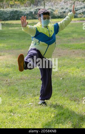 Eine asiatisch-amerikanische Frau, die eine Gesichtsmaske und einen Schild trägt. An einem Tai Chi Kurs im Kissena Park, Flushing, Queens, New York City. Stockfoto