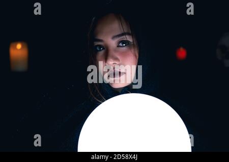 Porträt des asiatischen Wahrsager in schwarzer Kapuze mit heller Kristallkugel. Stockfoto