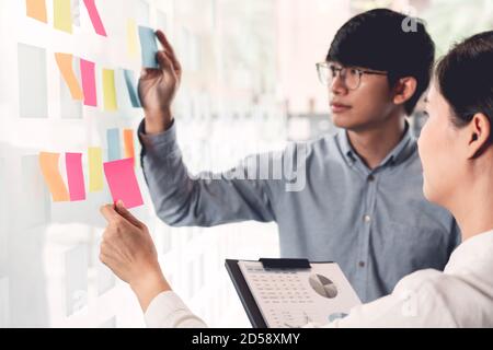 Business Manager zeigen Idee für ihr Team und kleben viele Memo-Papier auf Glasfenster zum Erfolg Arbeit in Business Meeting Kreativbüro, Planung Stockfoto