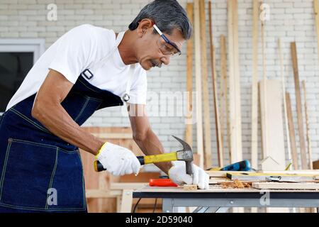 Asiatische Senior Mann Nagel Holzbrett in Schreinerei Werkstatt. Konzept Senioren Hobby nach dem Ruhestand. Stockfoto