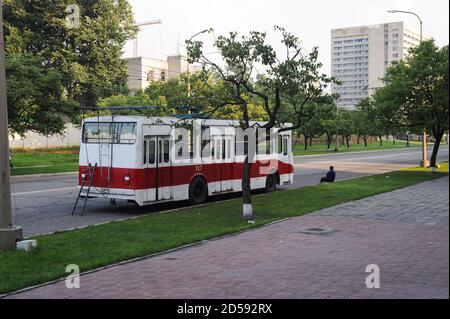 08.08.2012, Pjöngjang, Nordkorea, Asien - EIN Mann sitzt neben einem zerbrochenen Trolleybus am Straßenrand im Zentrum der nordkoreanischen Hauptstadt. Stockfoto