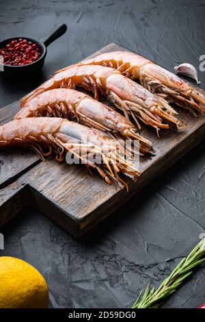 Meeresfrüchte-Garnelen auf Holzschneidebrett mit Gewürzen, Pfeffer und Zitrone auf schwarzer Betonoberfläche Stockfoto