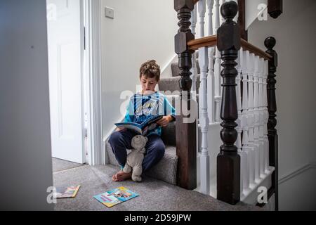 Sechs Jahre alter Junge, der ein Buch las, während er auf seiner Wohntreppe saß, England, Vereinigtes Königreich Stockfoto